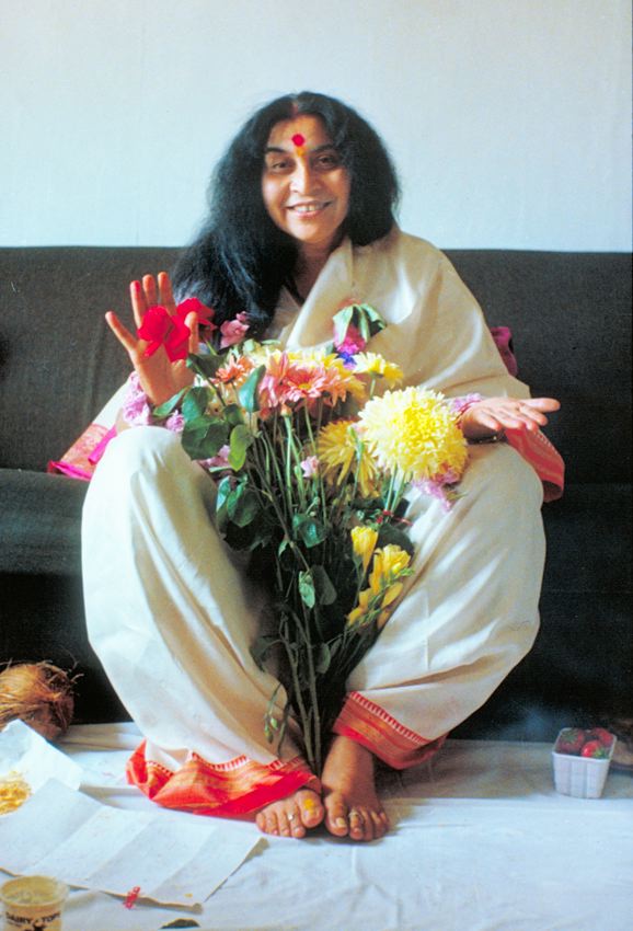 Shri Mataji Nirmala Devi sitting with flowers on a sofa in the United Kingdom